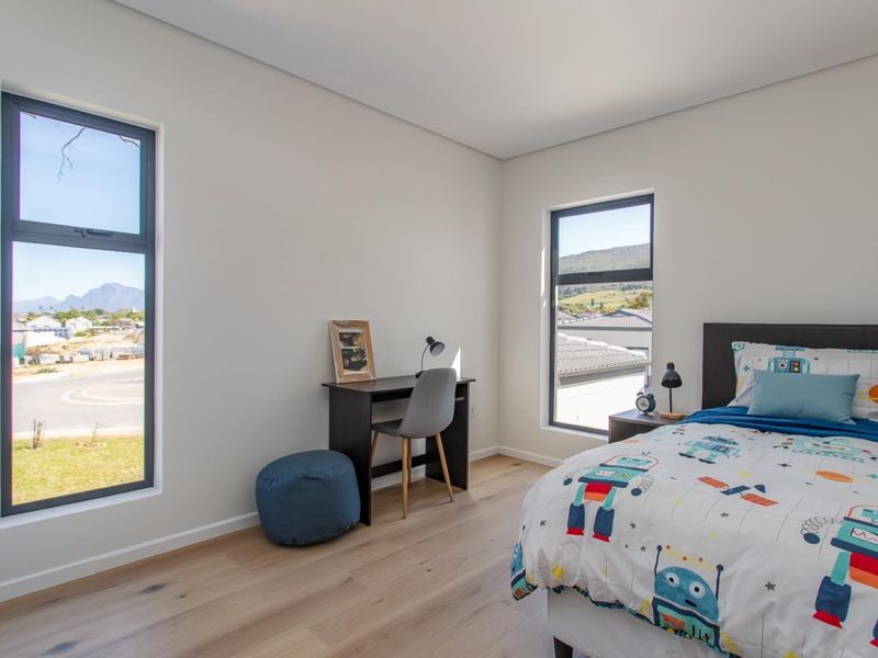 A bright and modern bedroom featuring light laminate flooring and large aluminium-framed windows with views of the surrounding neighbourhood.