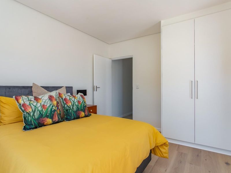 A bright and modern bedroom featuring light laminate flooring, neutral walls, and a clean, white built-in wardrobe.