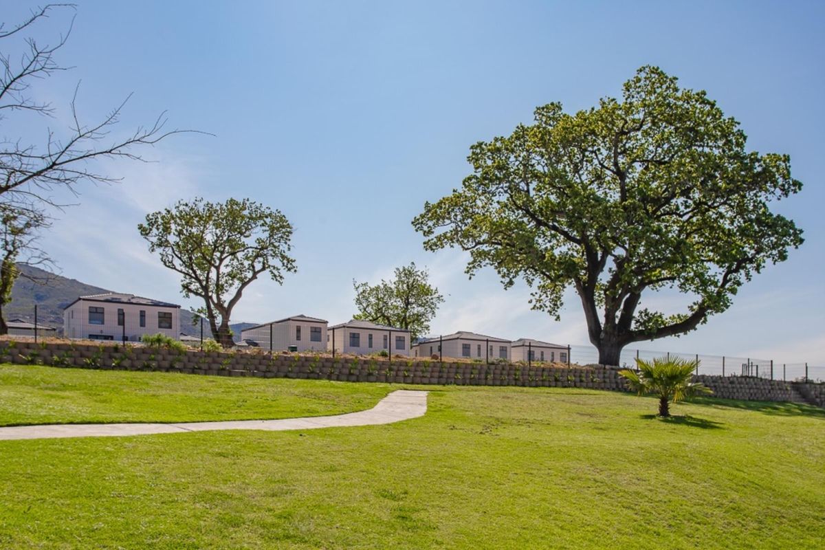 A view of the rear exterior of the townhouse complex, featuring a well-maintained lawn, paved walkway, and a stone retaining wall.