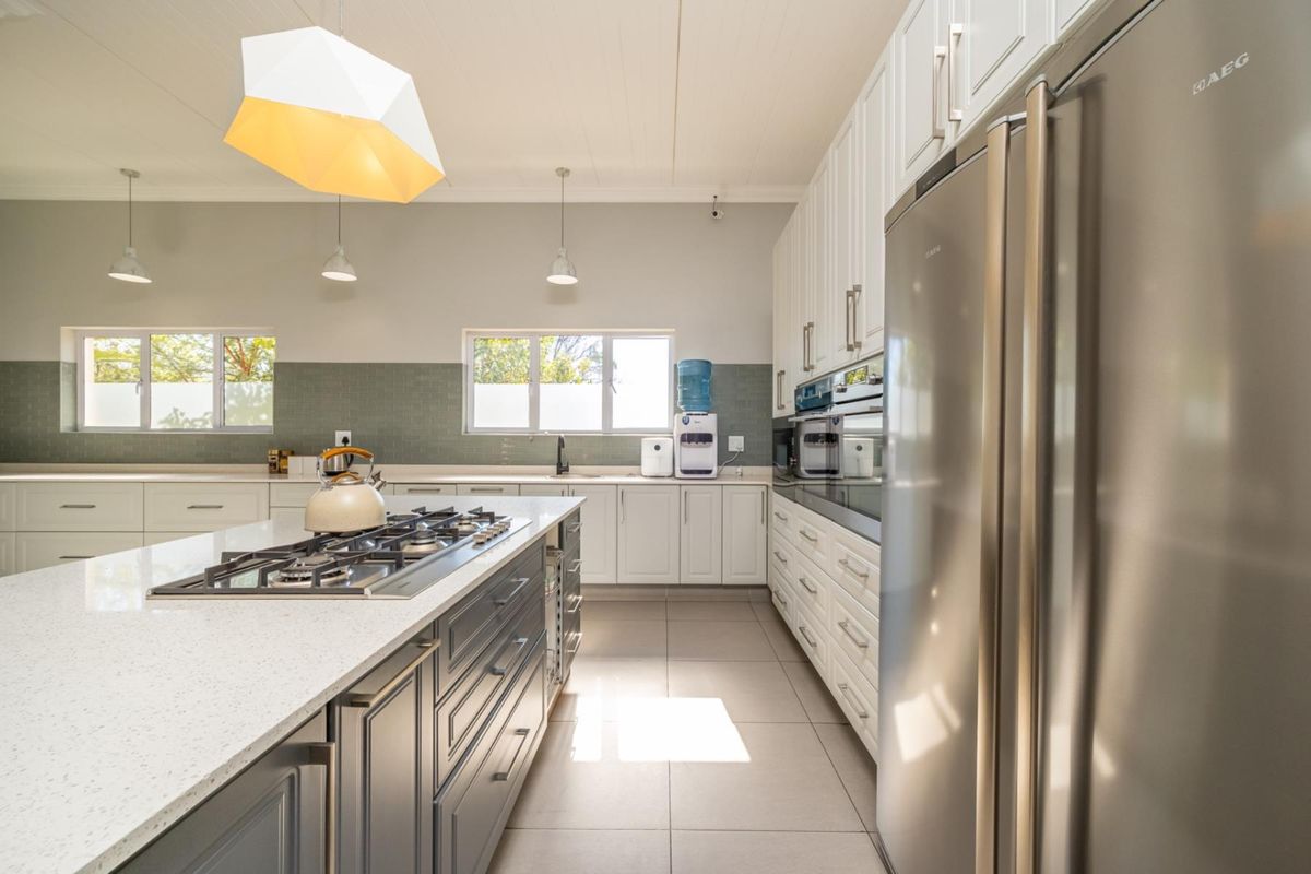 Modern kitchen featuring a large central island with gas cooktop, quartz countertops, shaker-style cabinetry, and high-quality tiled finishes.