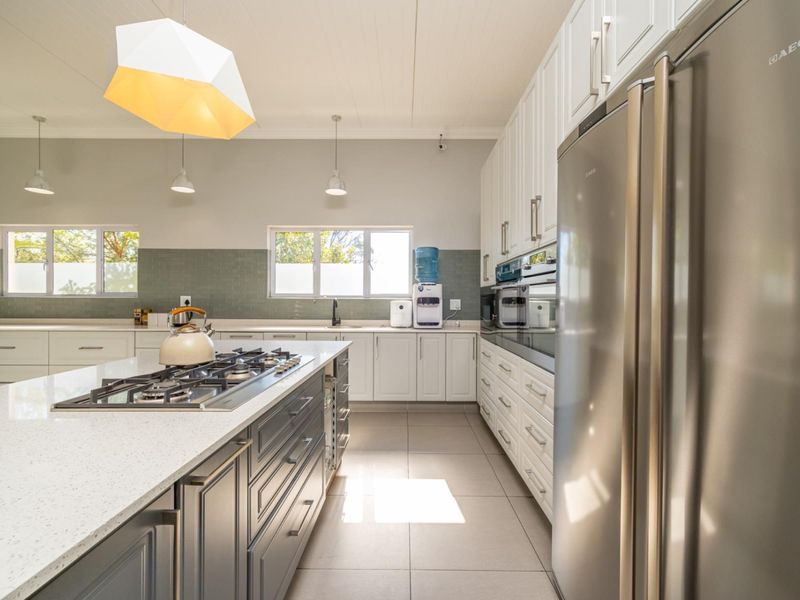 Modern kitchen featuring a large central island with gas cooktop, quartz countertops, shaker-style cabinetry, and high-quality tiled finishes.