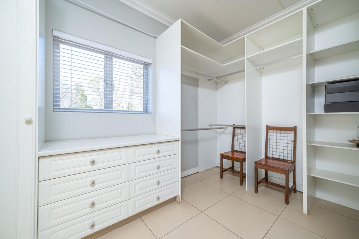 A clean and functional walk-in closet or dressing area featuring extensive built-in cabinetry, hanging rails, and neutral tiled flooring.