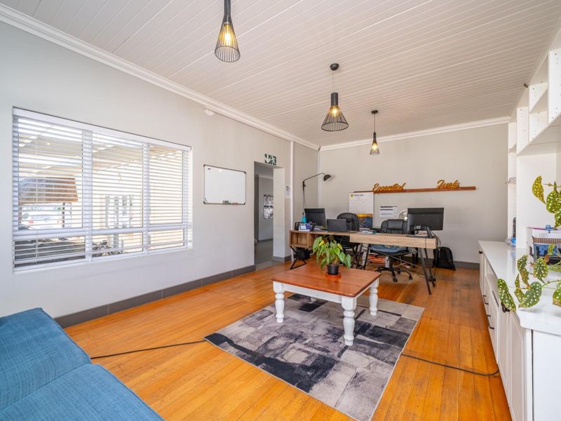 A bright home office featuring polished timber flooring, tongue and groove ceiling, built-in shelving, and large windows with venetian blinds.