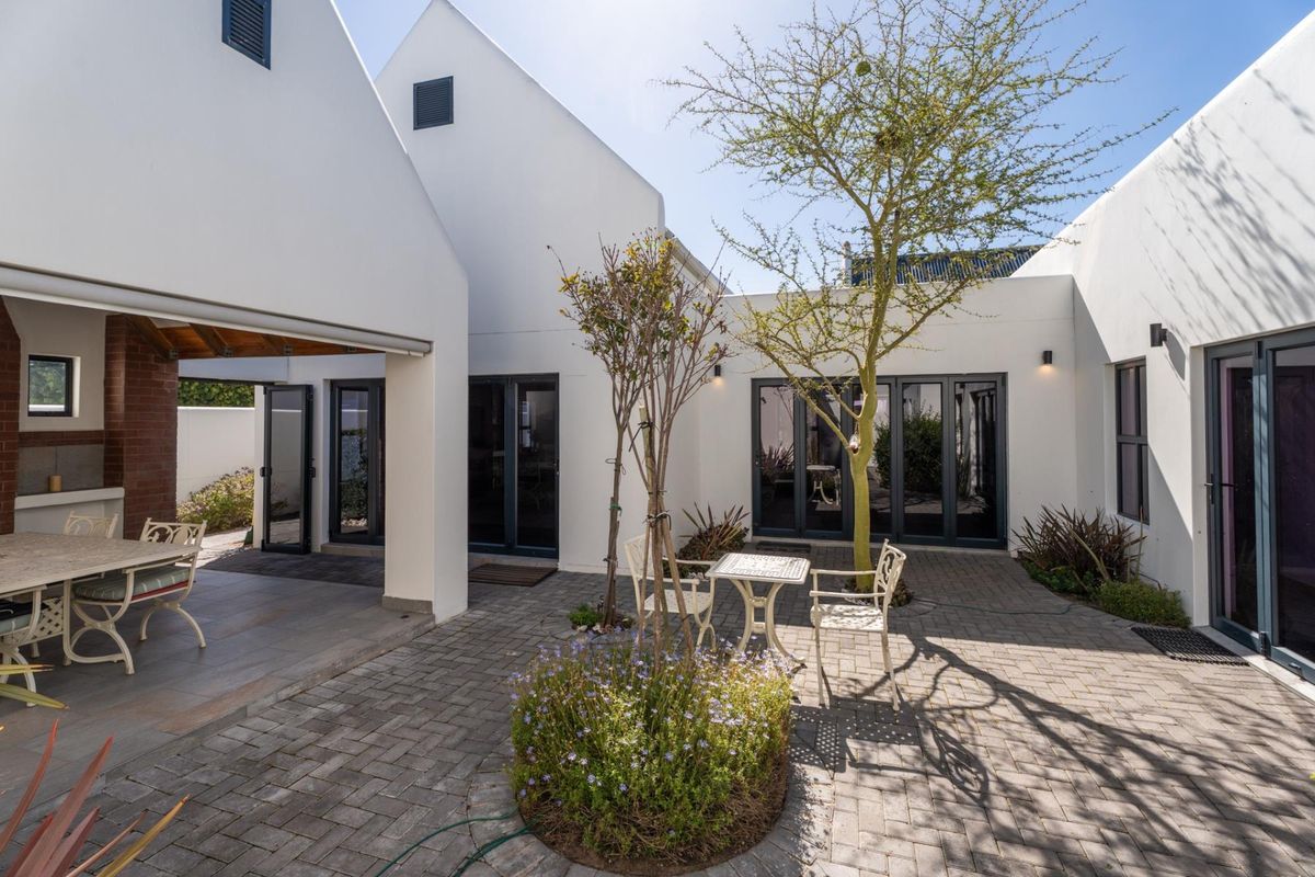 A well-maintained rear courtyard featuring a paved patio area, a covered outdoor entertainment space with a brick fireplace, and modern bi-fold doors.