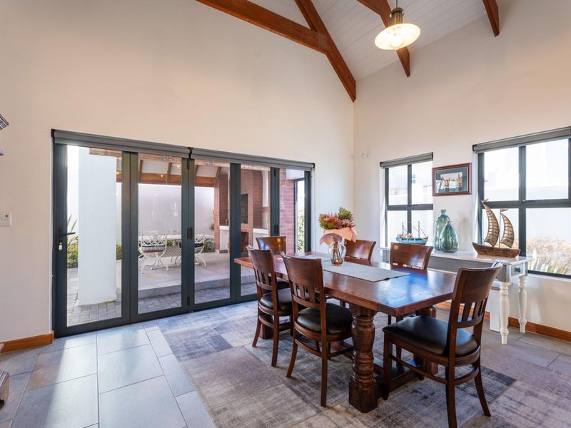 Spacious dining room featuring a vaulted ceiling with exposed timber beams, tiled flooring, and large bi-fold doors opening to an outdoor patio area.