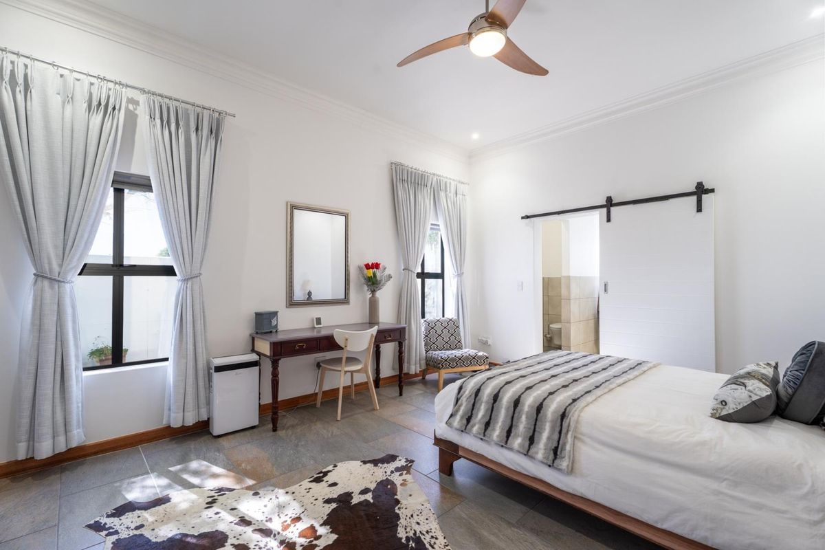A well-maintained bedroom featuring tiled flooring, crown molding, a ceiling fan, and a sliding barn door leading to an en-suite bathroom.