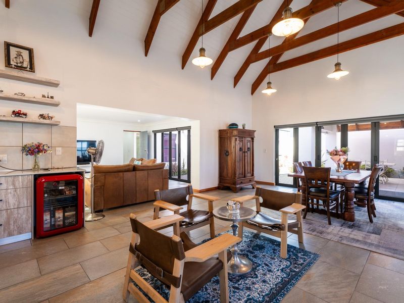 Spacious open-plan living and dining area featuring high vaulted ceilings with exposed timber trusses, tiled floors, and large bi-fold doors leading to the outdoors.