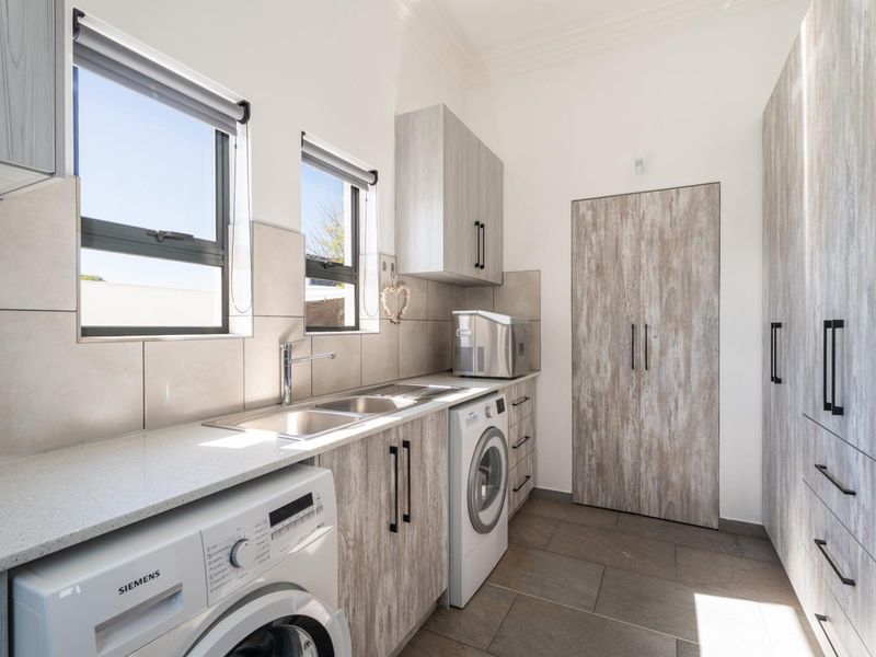 Modern, well-appointed laundry room featuring sleek wood-grain cabinetry, stone countertops, a double sink, and integrated appliance spaces with tiled flooring.