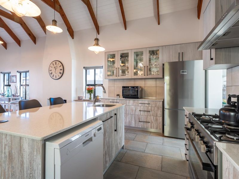 Modern kitchen featuring a large island with stone countertops, gas stove, ample cabinetry, and high vaulted ceilings with exposed timber beams.