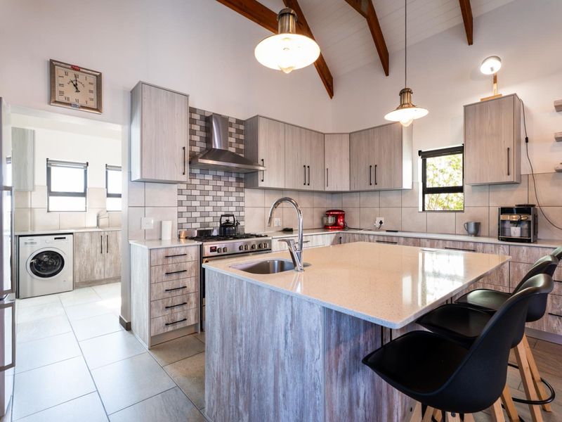 Modern kitchen featuring a central island with stone countertops, gas stove, extractor fan, and exposed timber beams, with an adjacent laundry area.