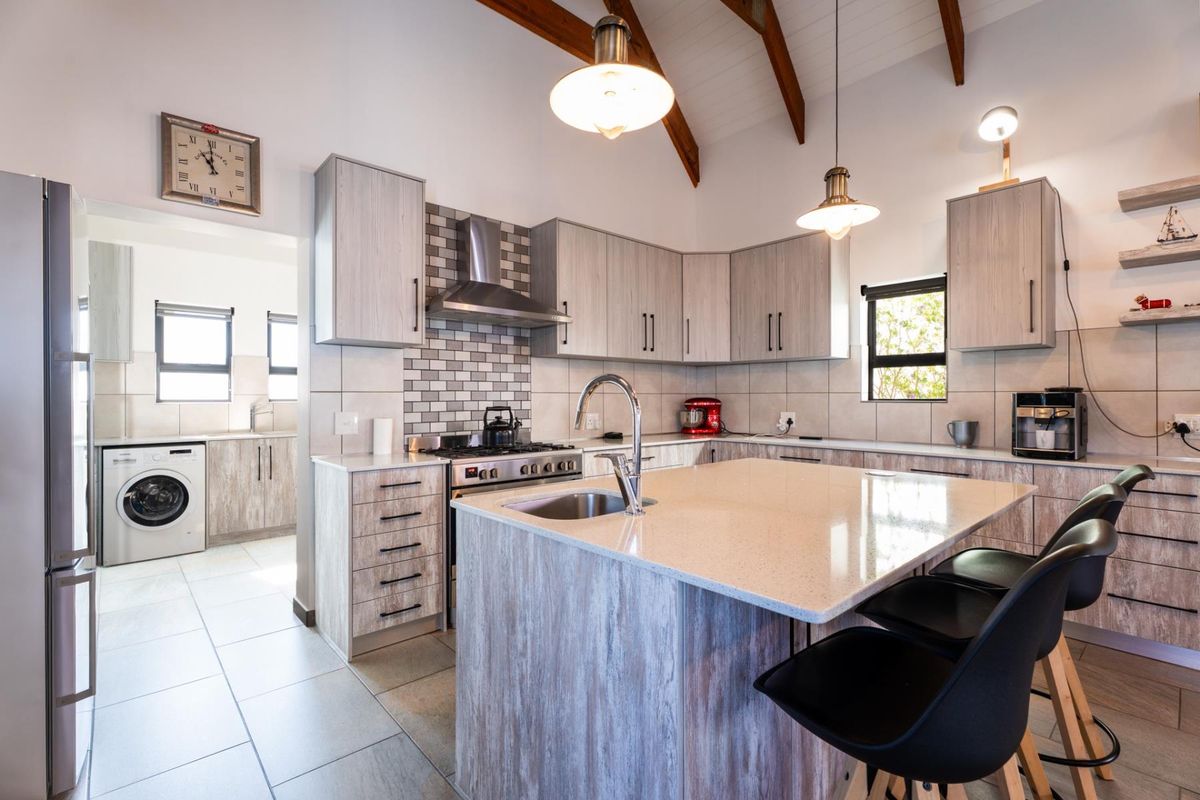 Modern kitchen featuring a central island with stone countertops, gas stove, extractor fan, and exposed timber beams, with an adjacent laundry area.