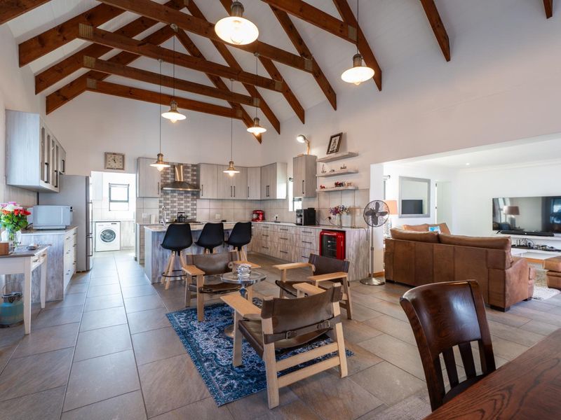 Spacious open-plan living and kitchen area featuring a high vaulted timber beam ceiling, modern cabinetry, and large format floor tiles.
