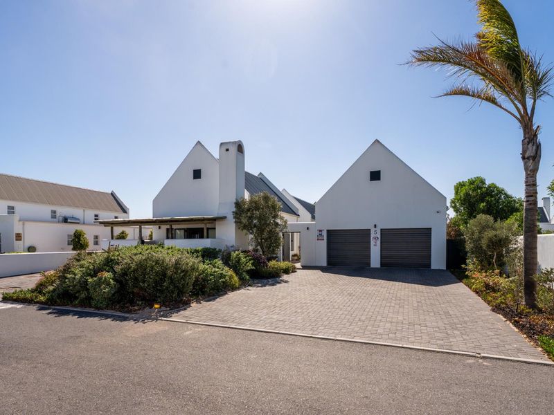 A well-maintained modern house featuring a double garage, paved driveway, and a distinctive white facade with a prominent chimney.