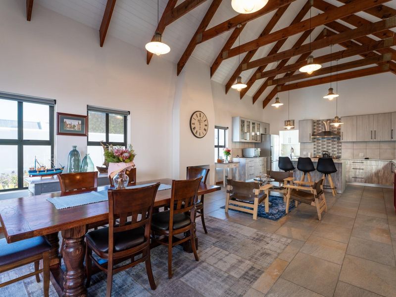 Spacious open-plan living and dining area featuring high vaulted ceilings with exposed timber trusses, tiled floors, and a modern kitchen with a central island.