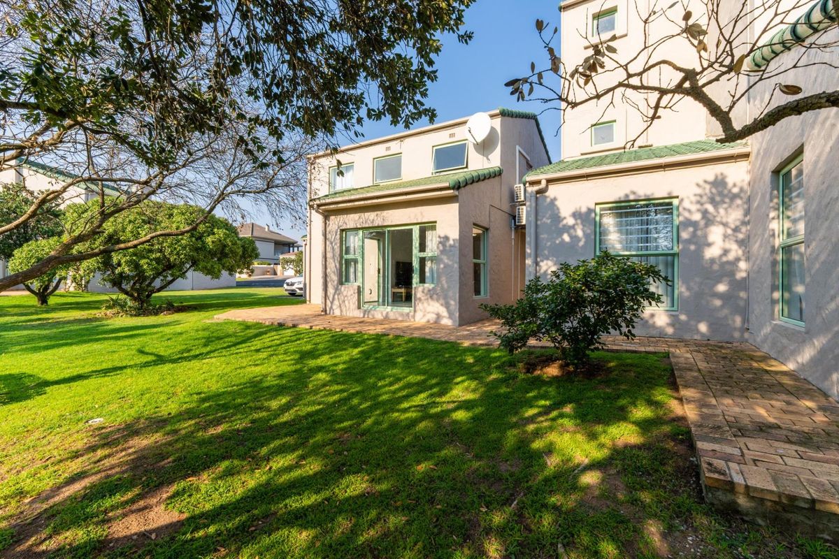 Rear view of the apartment building featuring a brick paved patio area, well-maintained lawn, and sliding glass door access.