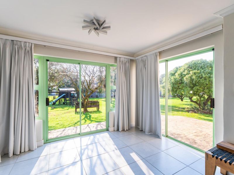 Bright living area featuring large sliding glass doors that open onto a garden, with neutral tiled flooring and modern ceiling lighting.
