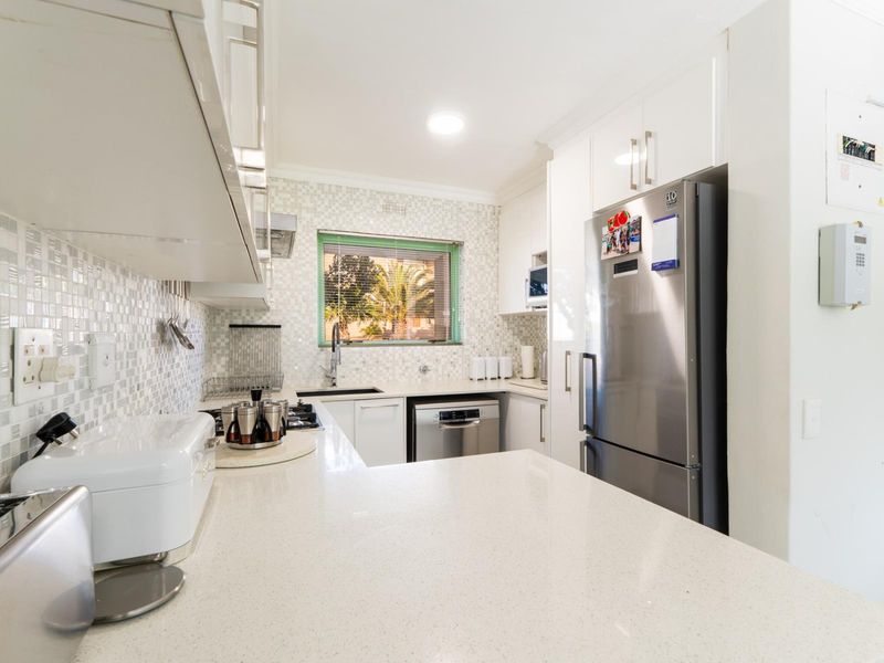 Modern kitchen featuring white cabinetry, quartz countertops, mosaic tile backsplash, and integrated appliances, offering a clean and functional workspace.