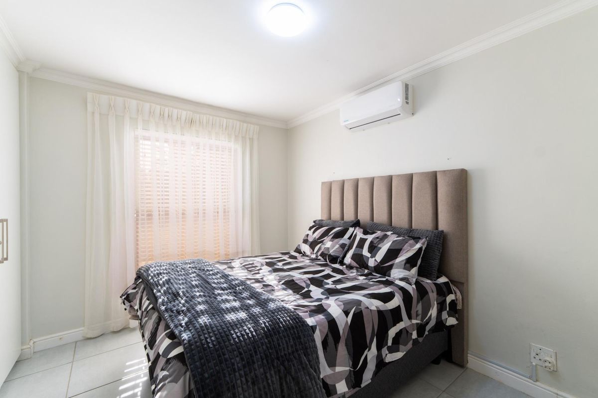 A well-maintained bedroom featuring tiled flooring, crown molding, and a wall-mounted air conditioning unit.