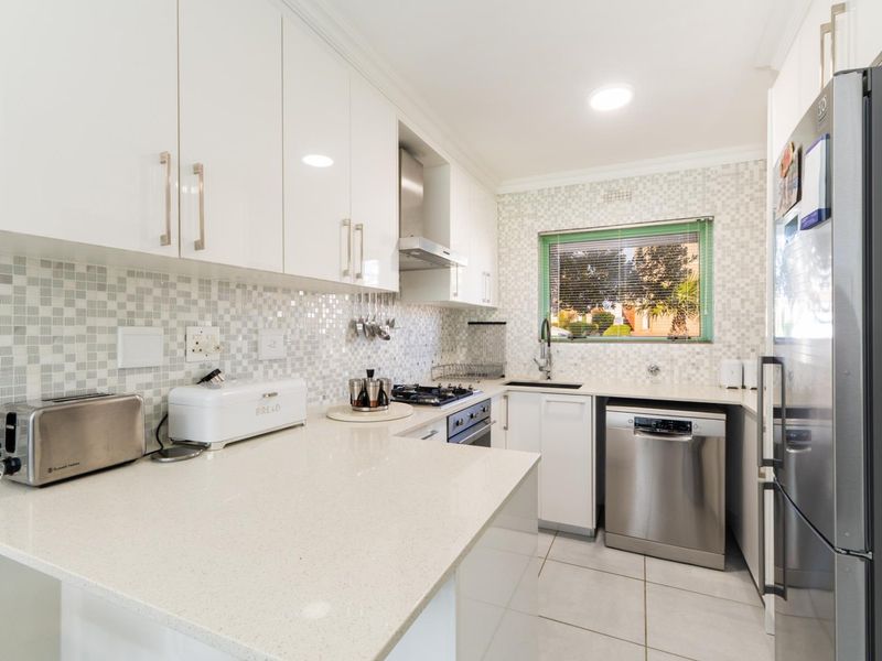 Modern kitchen featuring white high-gloss cabinetry, quartz countertops, mosaic tile backsplash, and integrated stainless steel appliances.