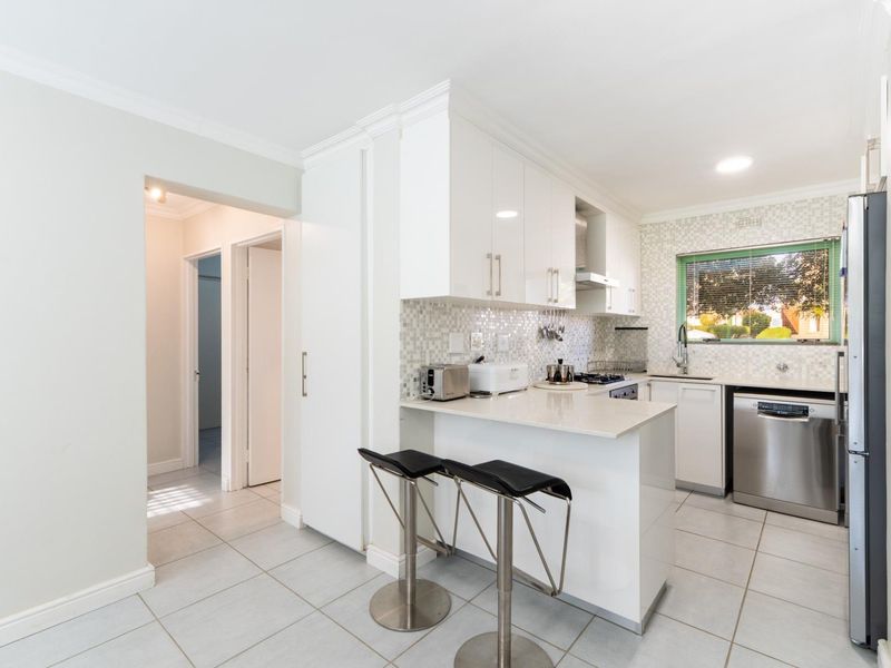 Modern kitchen featuring white high-gloss cabinetry, stone countertops, mosaic tile backsplash, and integrated stainless steel appliances with a breakfast bar.
