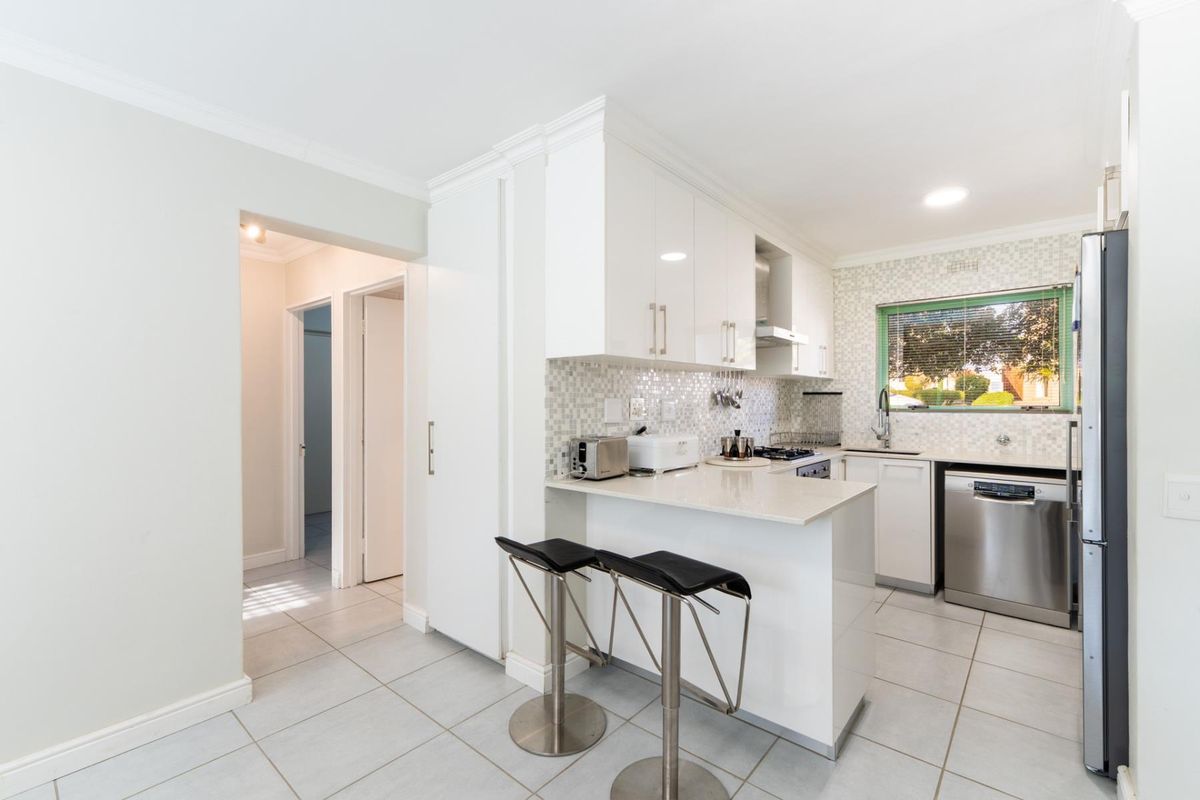 Modern kitchen featuring white high-gloss cabinetry, stone countertops, mosaic tile backsplash, and integrated stainless steel appliances with a breakfast bar.