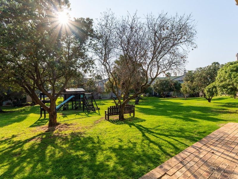 A well-maintained communal garden area featuring mature trees, expansive lawn space, and a paved walkway.