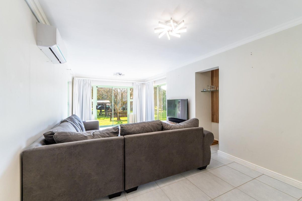 A bright living room featuring tiled flooring, a wall-mounted air conditioning unit, and sliding glass doors providing access to the garden.