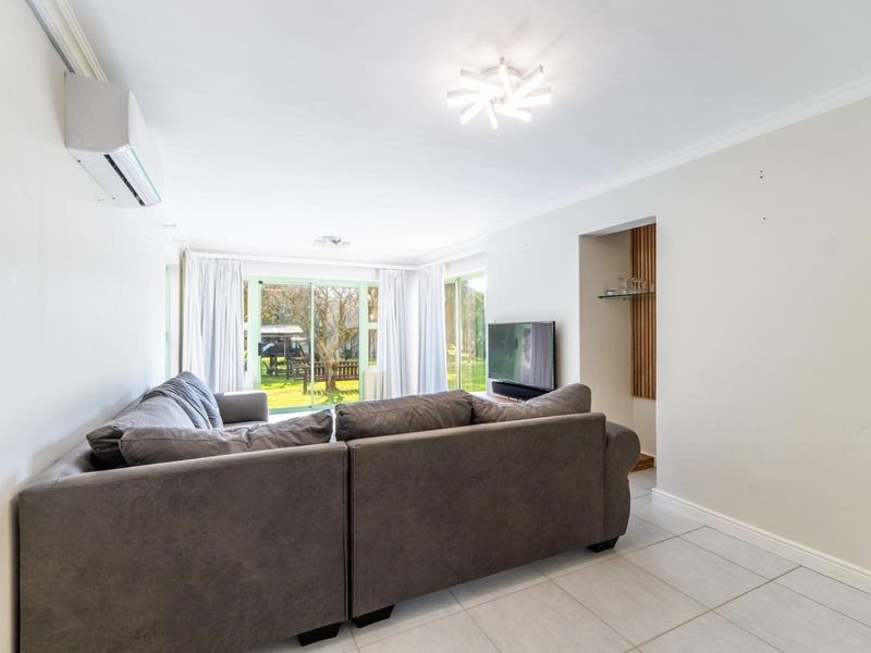 A bright living room featuring tiled flooring, a wall-mounted air conditioning unit, and sliding glass doors providing access to the garden.