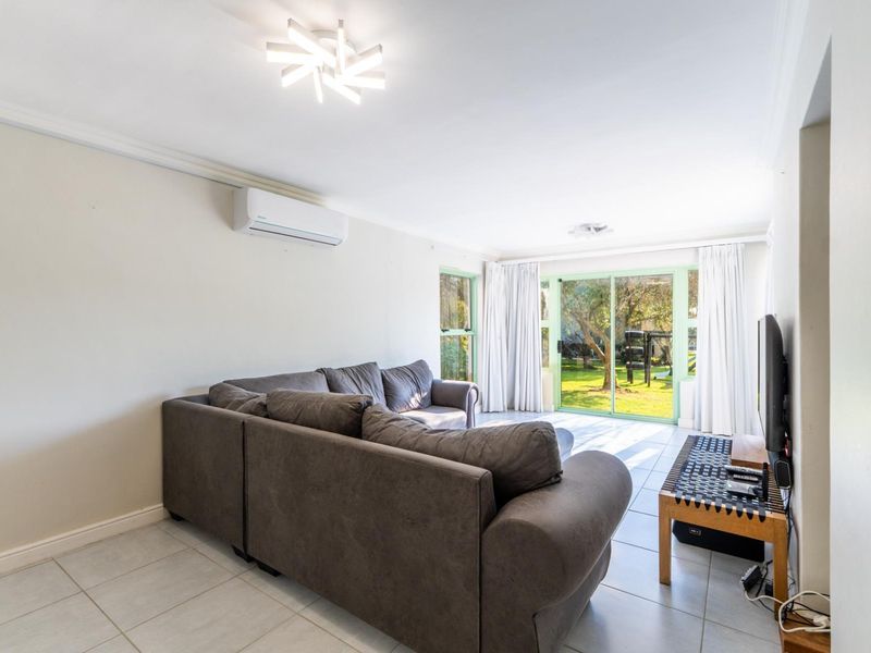 A bright living room featuring tiled flooring, a split-system air conditioner, and large sliding glass doors providing direct access to the garden.