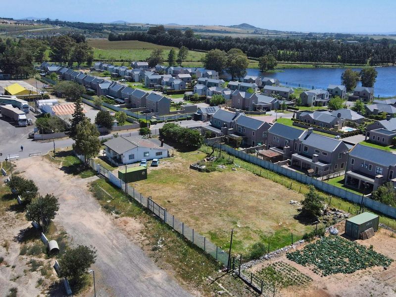 Aerial view of a vacant commercial land plot situated adjacent to a residential estate and a lake.