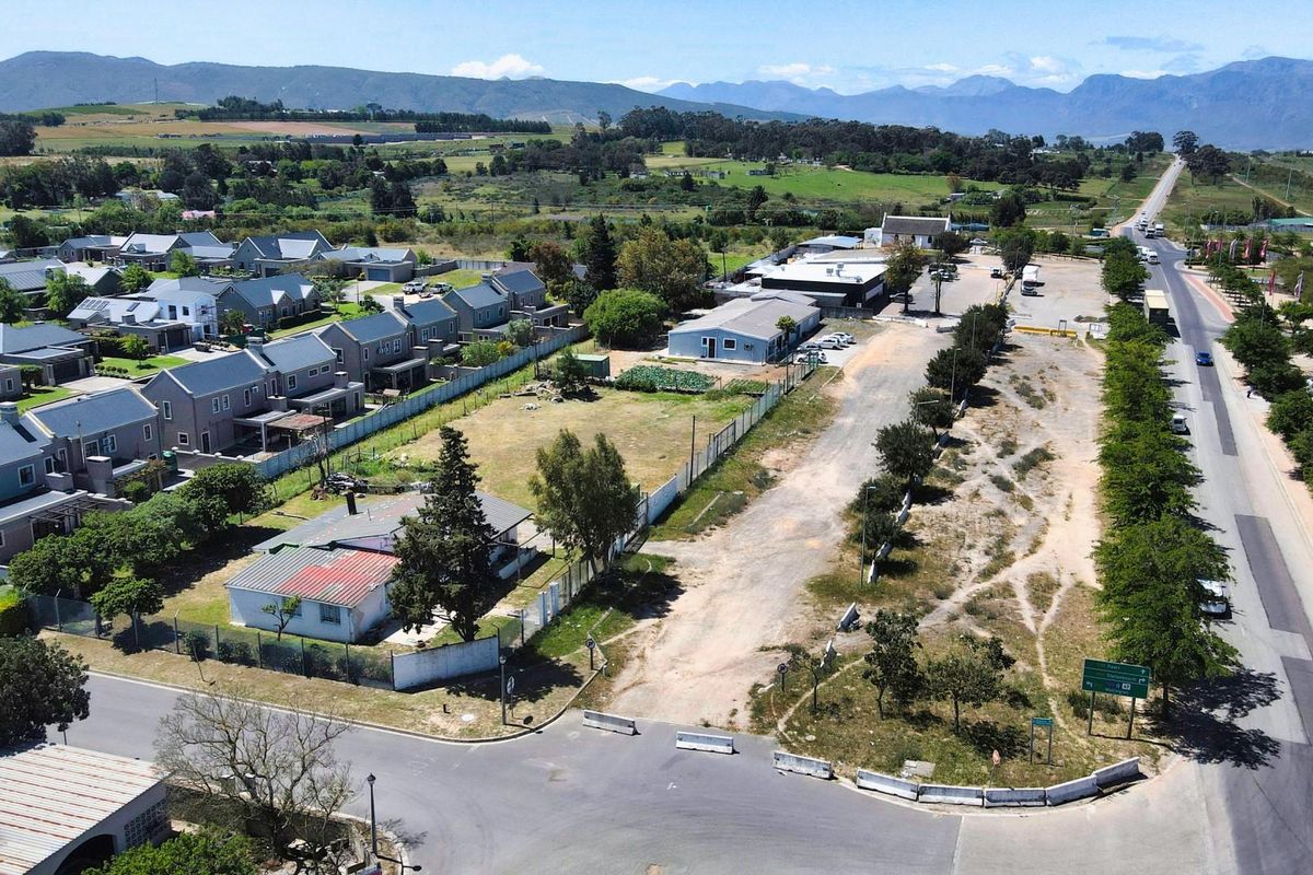 Aerial view of a commercial vacant land plot situated adjacent to a residential area and main road, offering significant development potential.
