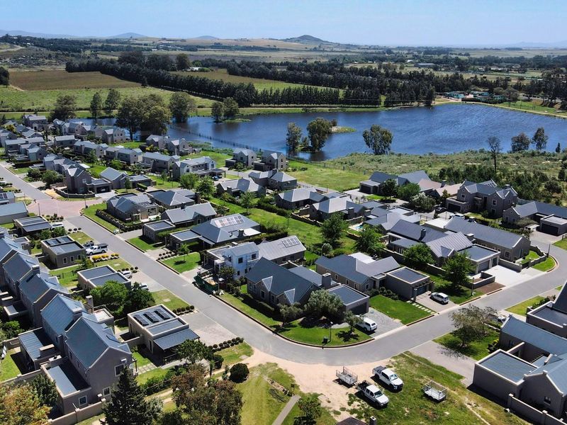 Aerial view of a residential estate featuring modern homes, paved streets, and a scenic lake in a well-maintained landscape setting.