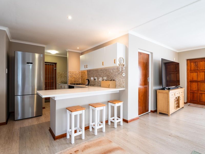 Open-plan living area featuring a modern kitchen with a breakfast bar, mosaic backsplash, and neutral finishes, seamlessly connecting to the main living space.
