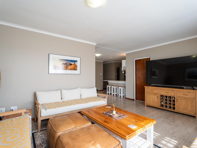 An open-plan living area featuring laminate flooring, neutral wall tones, and a seamless transition to the kitchen breakfast bar area.