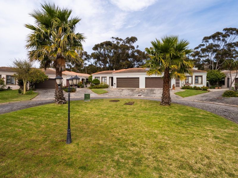 Front view of a townhouse complex featuring paved driveways, double garages, and well-maintained garden areas with mature palm trees.