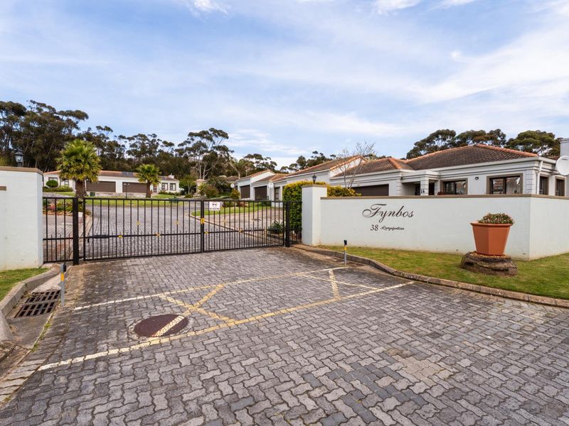 Front entrance view of Fynbos townhouse complex featuring a secure gated access point, paved driveway, and established residential units with tiled roofs.