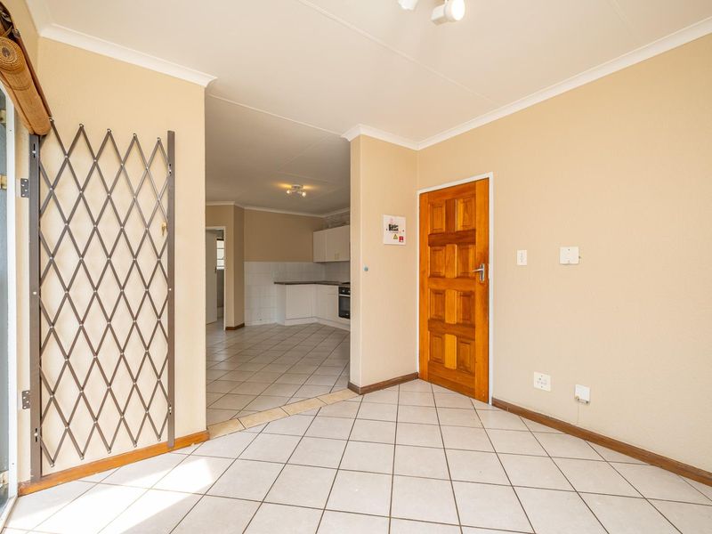 An entrance area featuring tiled flooring, a wooden door, and a security gate, leading into an open-plan kitchen space.