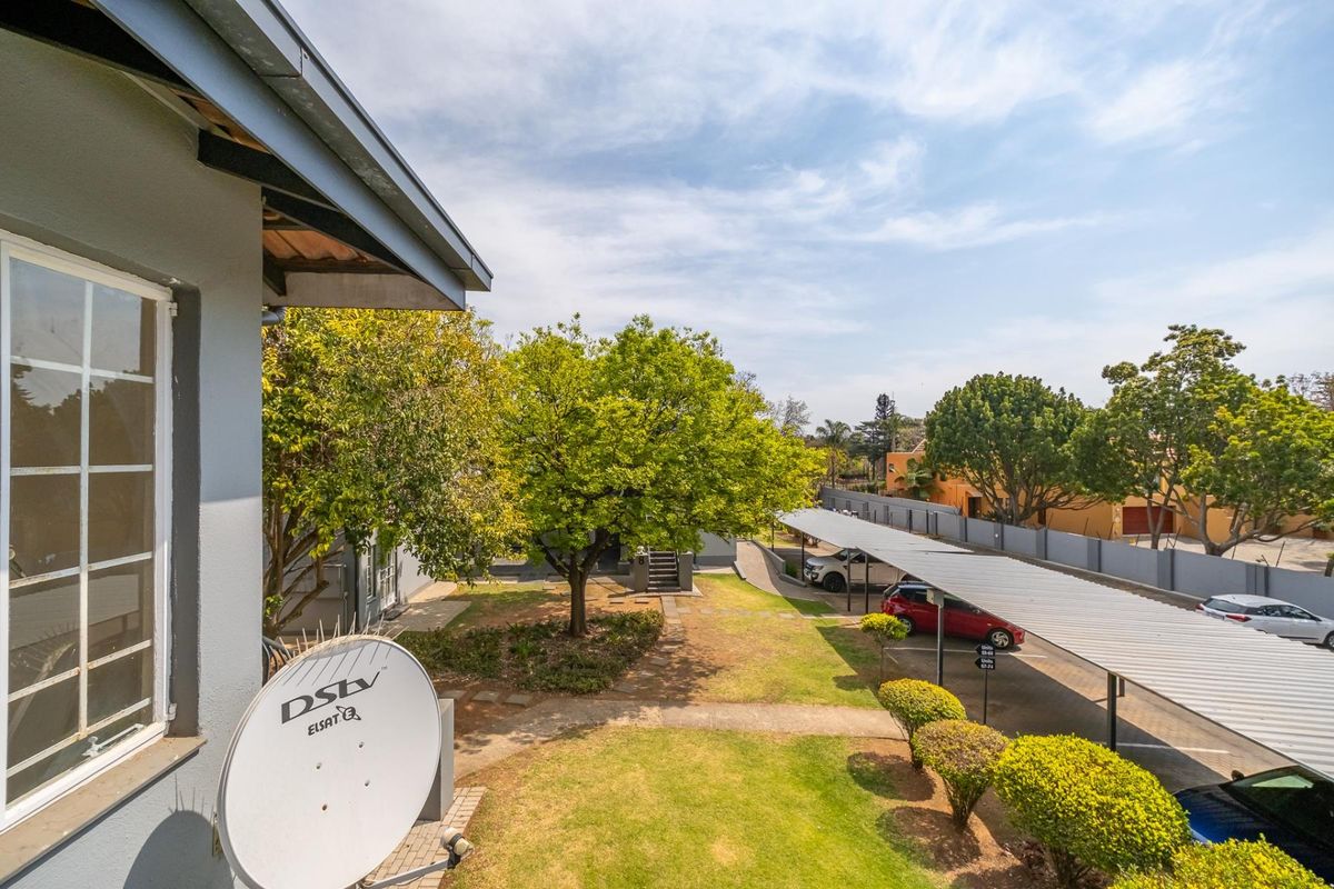 An elevated view of the apartment complex grounds, featuring a landscaped garden, paved pathways, and covered carport parking bays.