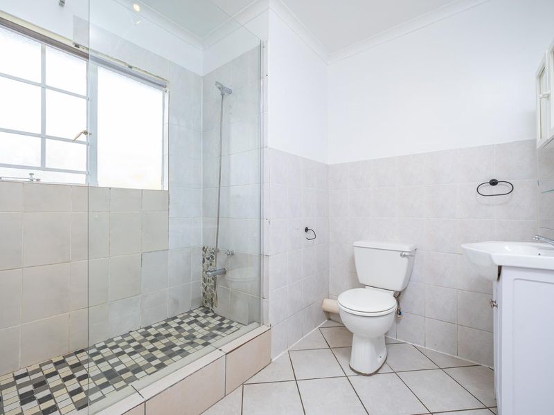 A functional bathroom featuring a glass-enclosed shower, pedestal basin, and toilet with neutral wall and floor tiling.