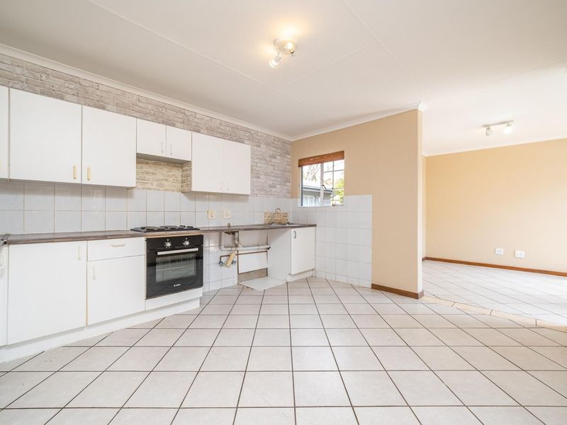 Open plan kitchen and living area featuring tiled flooring, white cabinetry, built-in oven and hob, and a neutral color palette.