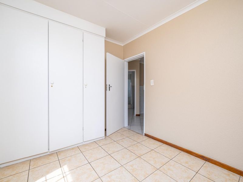 An empty bedroom featuring neutral wall paint, tiled flooring, and built-in cupboards, with a doorway leading to an adjacent room.