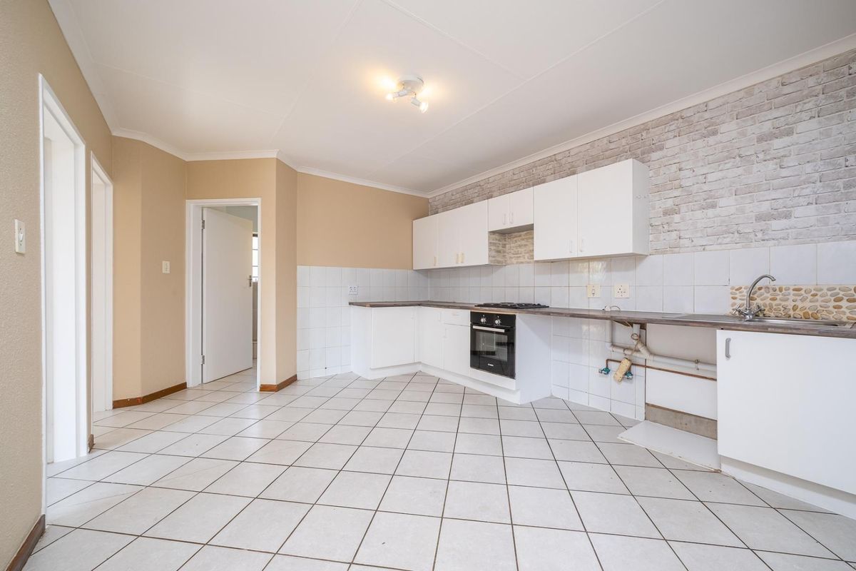 Empty kitchen featuring white cabinetry, built-in oven, hob, and tiled finishes. Requires minor repairs to plumbing and cabinetry to restore functionality.