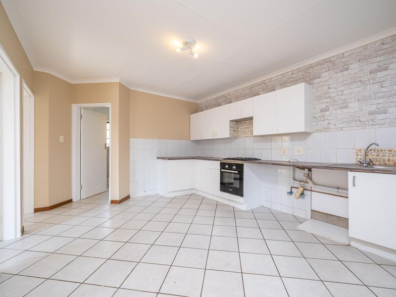 Empty kitchen featuring white cabinetry, built-in oven, hob, and tiled finishes. Requires minor repairs to plumbing and cabinetry to restore functionality.