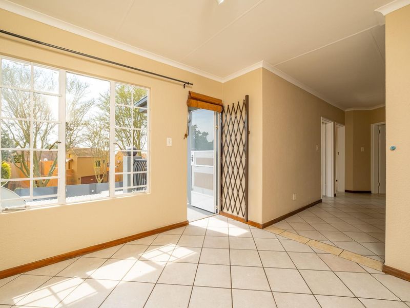 An empty, light-filled living area featuring tiled flooring, a security gate, and large windows leading to an outdoor space.