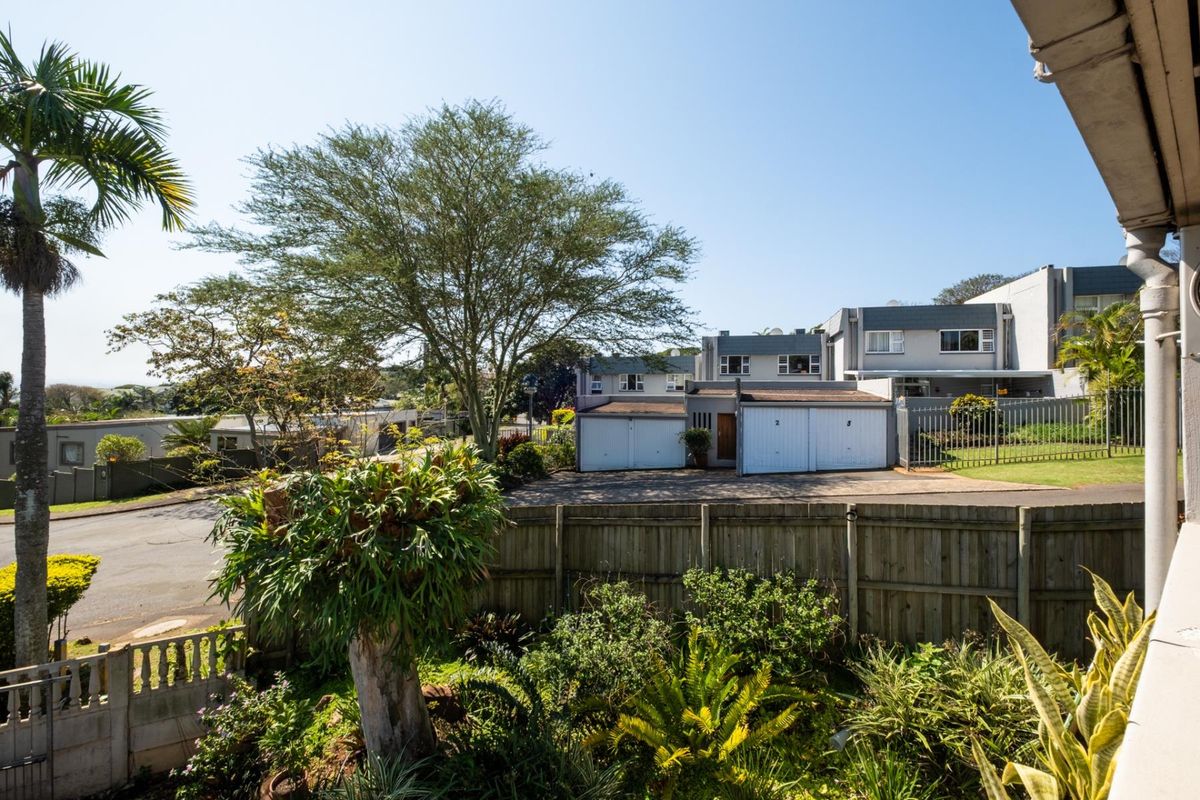 View of the rear garden area featuring a timber fence, established landscaping, and a view towards the neighbouring property's garages and driveway.