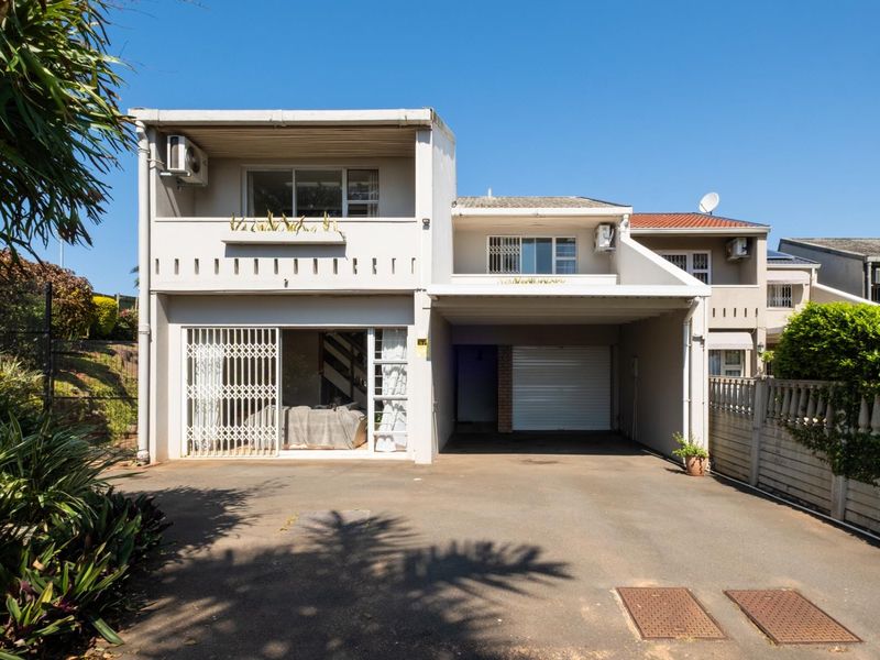 Front elevation of a two-story residential property featuring a paved driveway, integrated garage, and an upper-level balcony with security fixtures.
