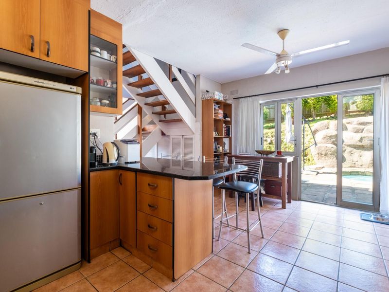 Open-plan kitchen and living area featuring wooden cabinetry, granite countertops, tiled flooring, and direct access to the rear patio through sliding glass doors.