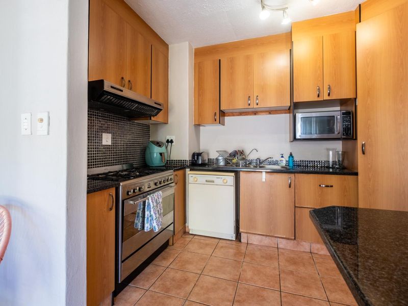 A functional kitchen featuring wooden cabinetry, granite countertops, a mosaic tile backsplash, and built-in stainless steel appliances with ceramic floor tiles.