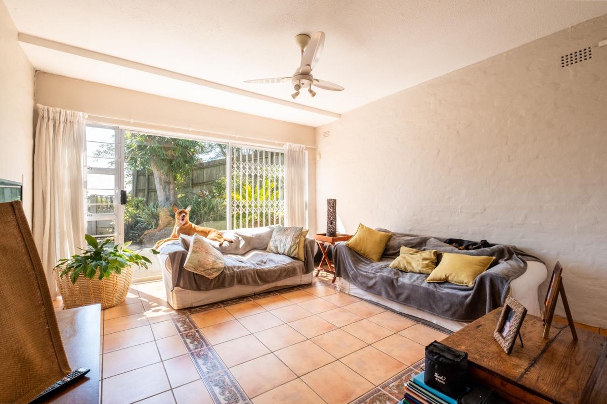 A bright living room featuring ceramic tile flooring, a ceiling fan, and large sliding glass doors providing direct access to the garden.