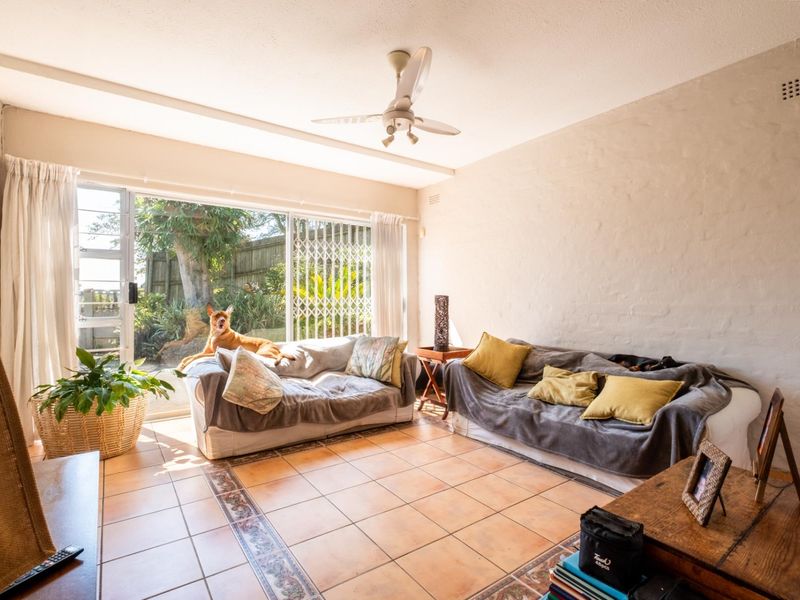 A bright living room featuring ceramic tile flooring, a ceiling fan, and large sliding glass doors providing direct access to the garden.